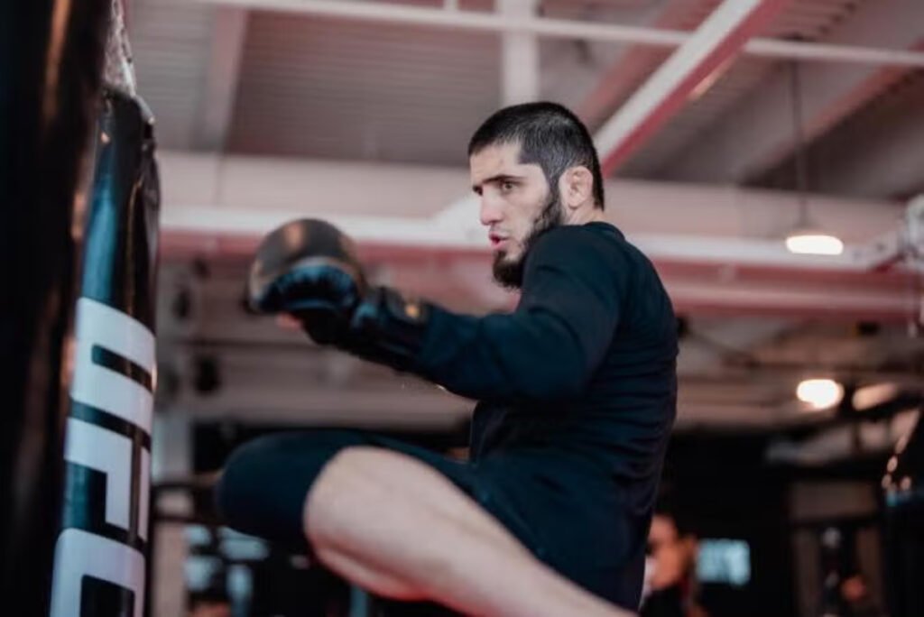 UFC fighter Islam Makhachev in black gear throws a knee strike at a heavy bag during a training session in a gym.