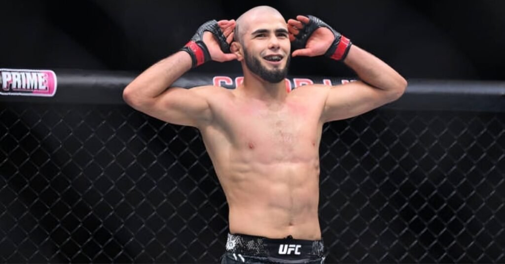 UFC fighter Muhammad Mokaev smiles in the octagon, posing with his hands raised to his head after a fight.