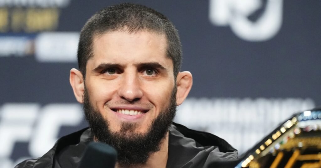 A smiling Islam Makhachev, the UFC Lightweight Champion, at a press conference with his title belt.
