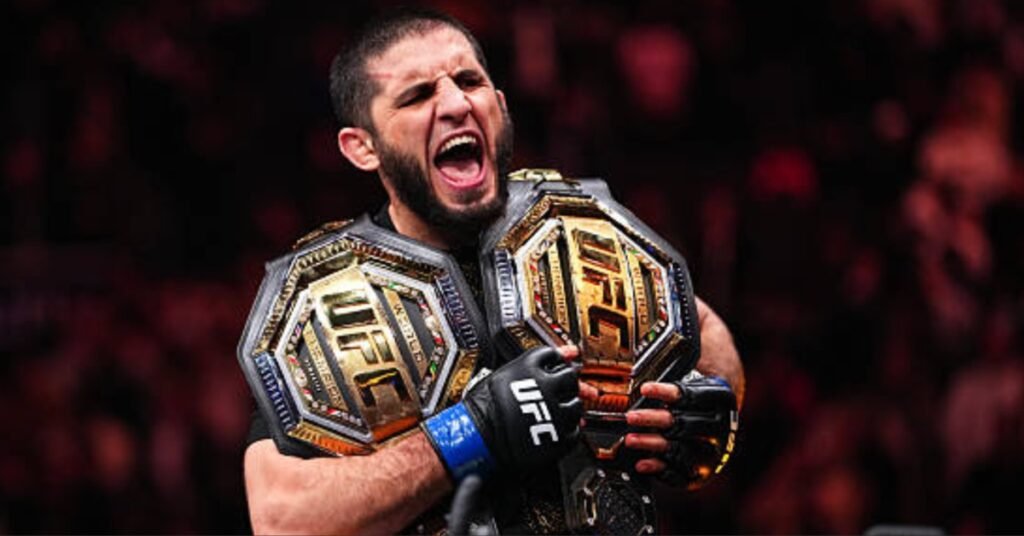 Islam Makhachev, campeón de UFC, grita de emoción sosteniendo dos cinturones de campeonato.