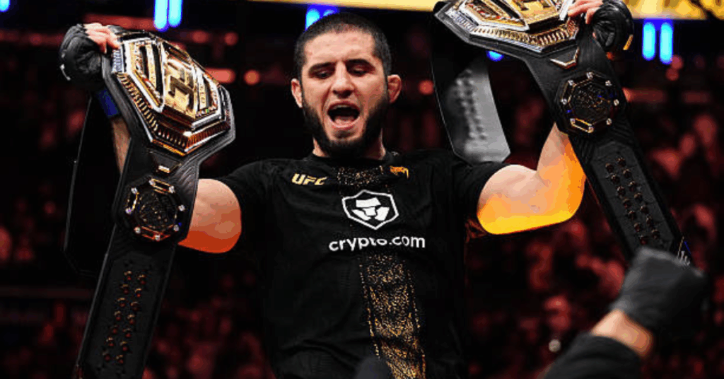 El campeón de la UFC Islam Makhachev celebra eufórico levantando dos cinturones.