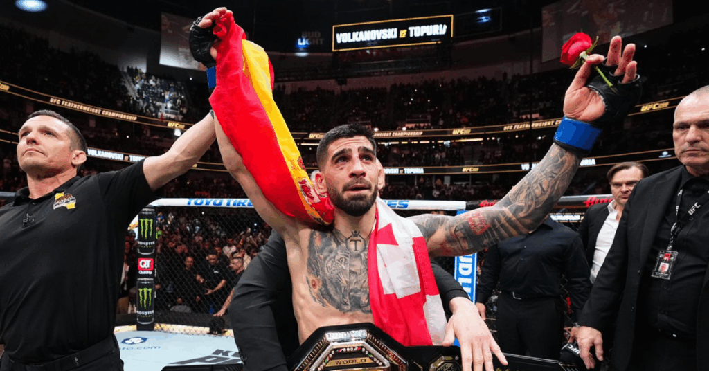 El luchador de UFC Ilia Topuria, emocionado, celebra su victoria con las banderas de España y Georgia y el cinturón de campeón.