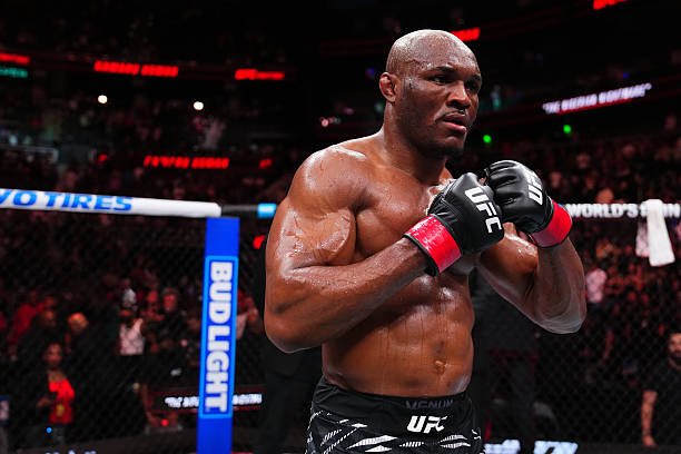 UFC fighter Kamaru Usman stands focused in the octagon with his gloved fists raised in a fighting stance.