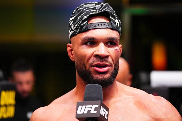 UFC fighter Kevin Lee, wearing a backward cap, speaks into a microphone during a post-fight interview.