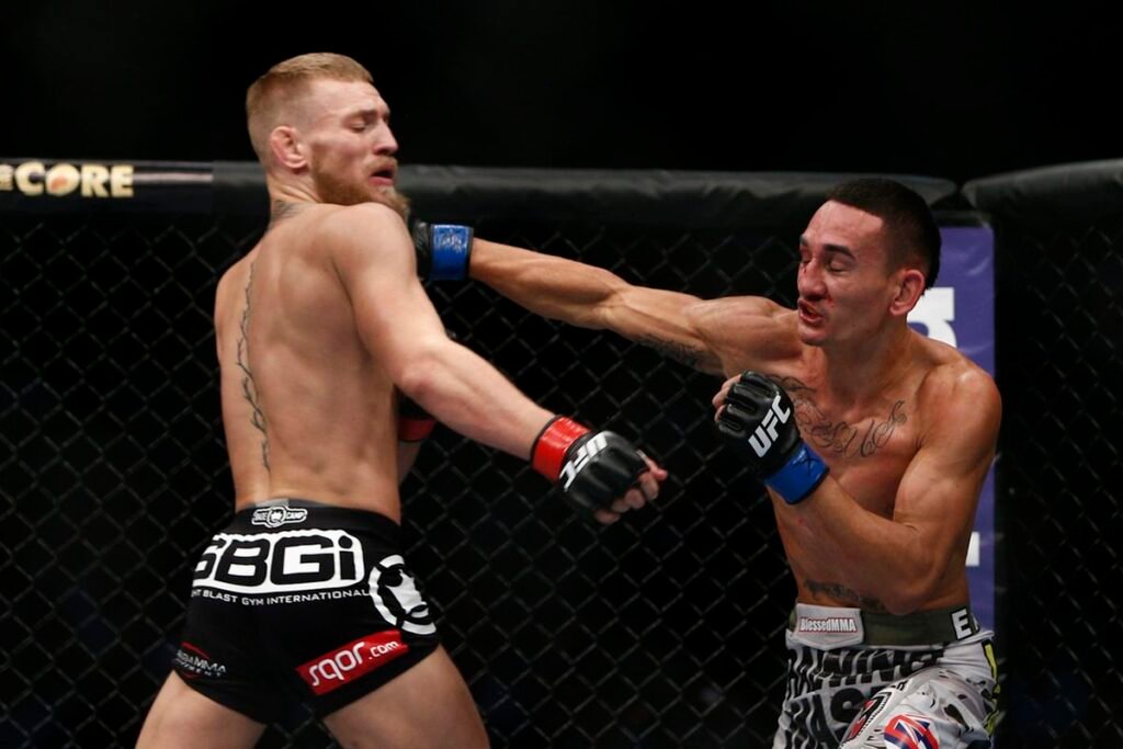 Combate UFC: Max Holloway golpea a Conor McGregor en la cabeza en el octágono. McGregor con mueca de dolor, Holloway con sangre en la cara.