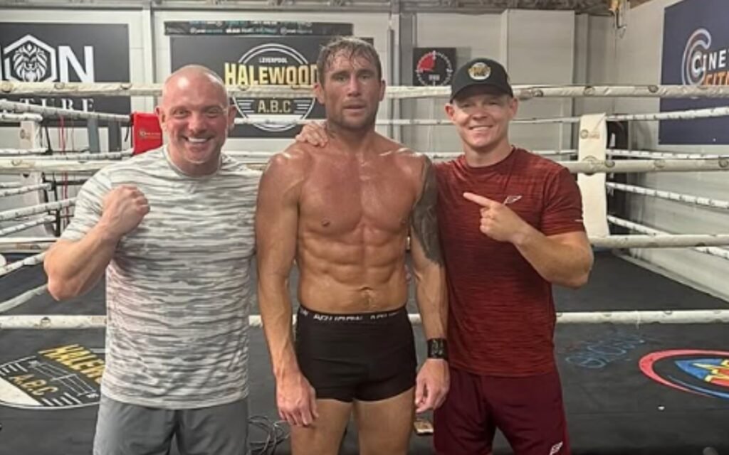 Darren Till, musculoso y sudoroso, junto a dos hombres sonrientes en un ring de boxeo de Liverpool.