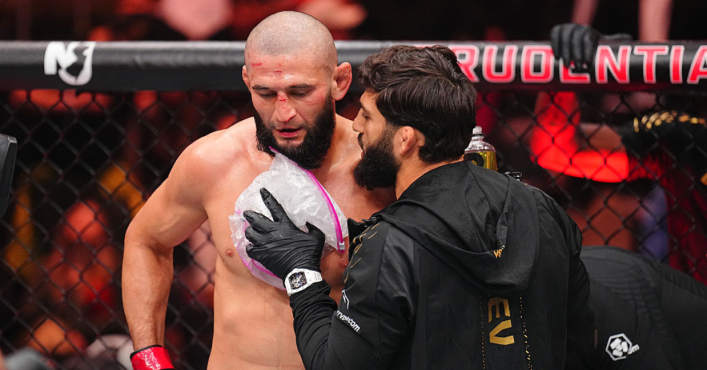 Luchador de MMA con heridas faciales recibe un paquete de hielo del equipo de esquina dentro de la jaula tras un combate.