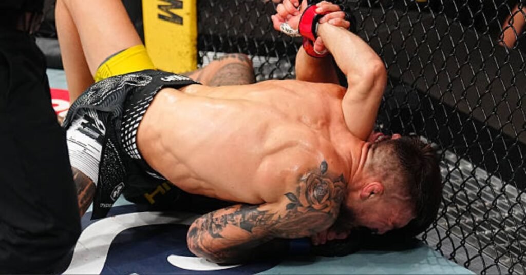 Luchador de MMA en el suelo del octágono, exhausto o con dolor, brazos arriba tras un intenso combate.