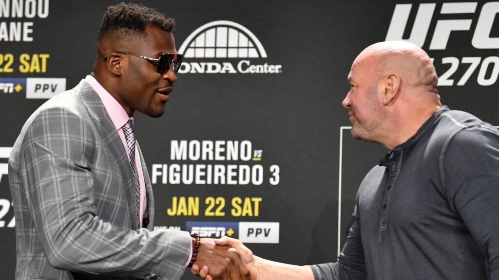 Francis Ngannou (traje a cuadros y gafas de sol) y Dana White se estrechan las manos en un evento de prensa de UFC.