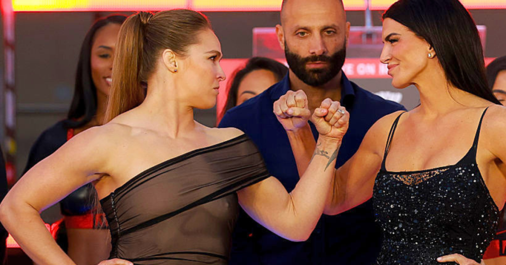 Ronda Rousey y Raquel Pennington se encaran tensas en un evento. Un hombre barbudo observa la confrontación entre las luchadoras de MMA.