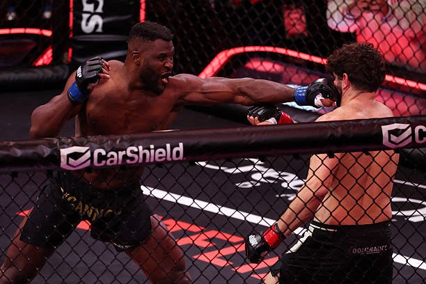 Francis Ngannou lanza un puñetazo impactante a su oponente en pleno combate de MMA, en la jaula de CarShield.