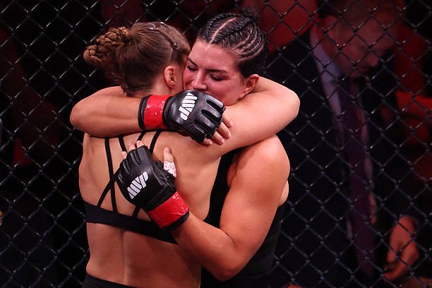 Tras el combate de MMA, dos luchadoras se funden en un abrazo emotivo dentro de la jaula. Guantes de lucha MVP.