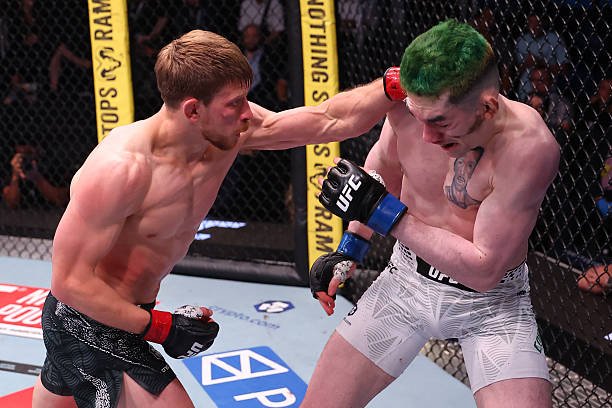 Luchador de MMA lanza un gancho de izquierda a la cabeza de su rival de cabello verde en el octógono de UFC.