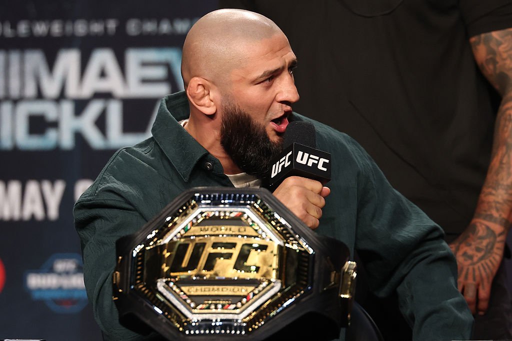 Khamzat Chimaev, con barba y cabeza afeitada, habla en un micro UFC junto a su cinturón de campeón.