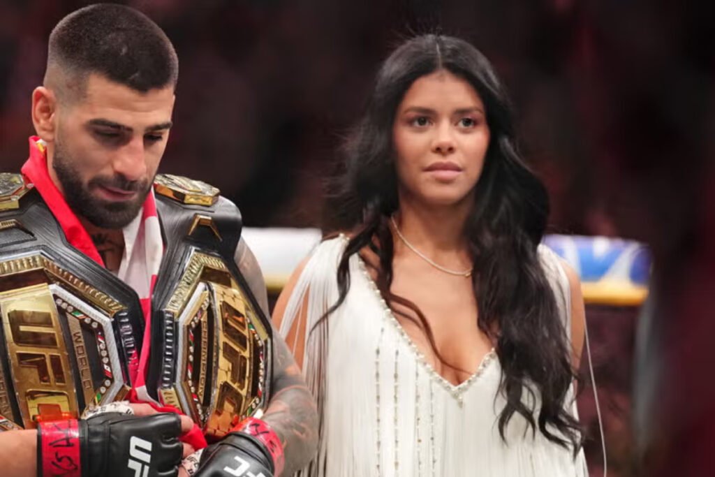 El campeón UFC Ilia Topuria con cinturones y guantes MMA, junto a Giorgina Uzcategui de vestido blanco y flecos.