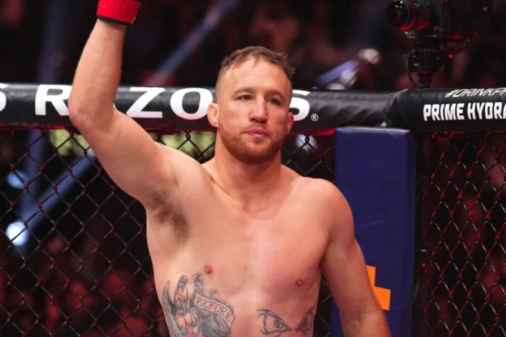 Luchador Justin Gaethje en el octágono de la UFC, brazo izquierdo alzado con guante rojo y tatuajes visibles.