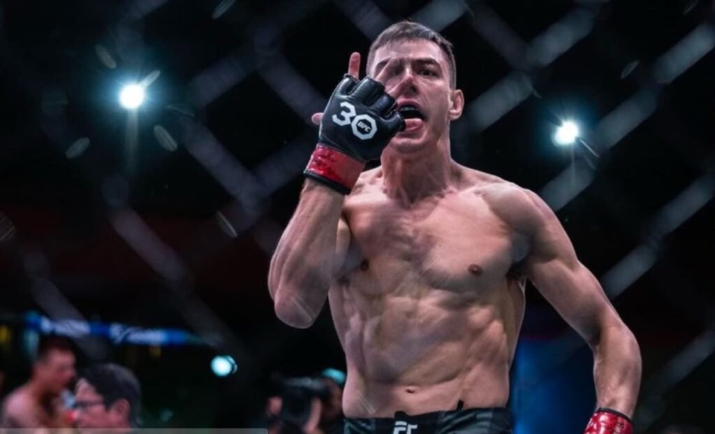 Luchador UFC Manuel Torres celebra en la jaula, torso musculoso, guante 30, sacando la lengua y haciendo un gesto shaka.