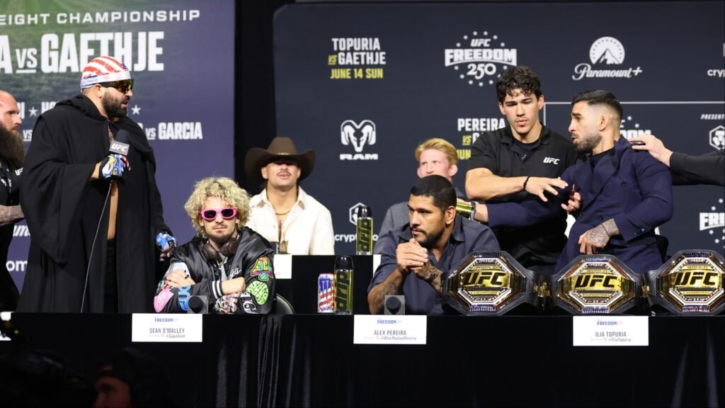 Rueda de prensa UFC con Sean O'Malley, Alex Pereira e Ilia Topuria. Varios cinturones de campeón sobre la mesa.