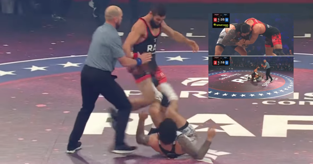 Lucha libre: un luchador de rojo y negro controla a su oponente en el suelo. Árbitro cercano. Mat Ramfight estrellado. Pantallas de marcador.