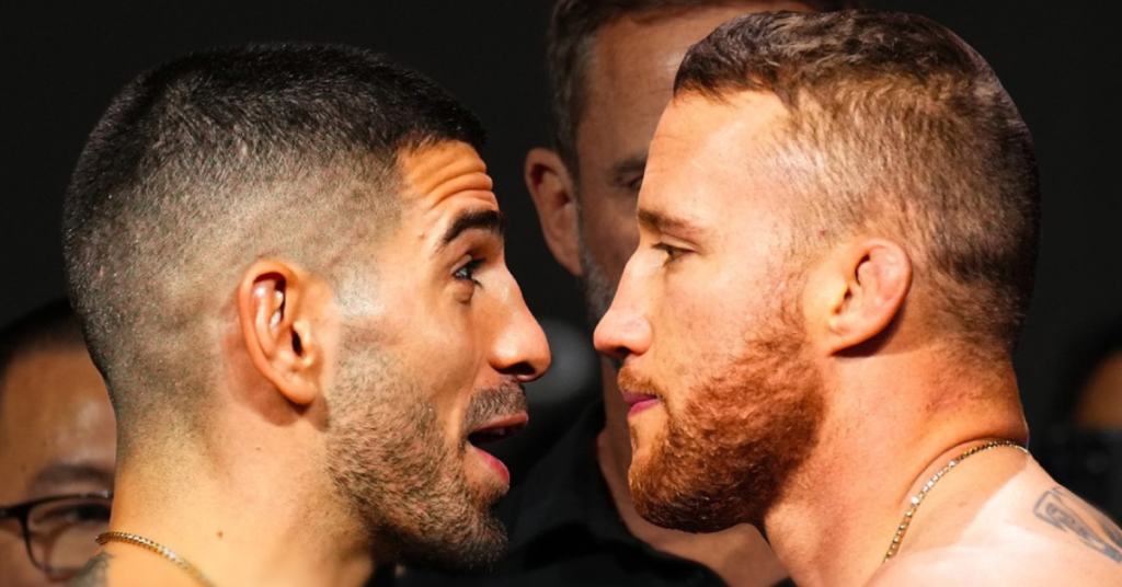 Dos luchadores de MMA, uno con barba oscura y otro rojiza, se encaran intensamente. Cadenas de oro y máxima tensión.