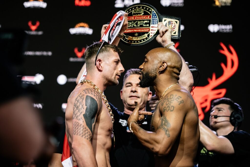 Intenso careo entre dos luchadores de BKFC, con un árbitro separándolos y un cinturón de campeón levantado.