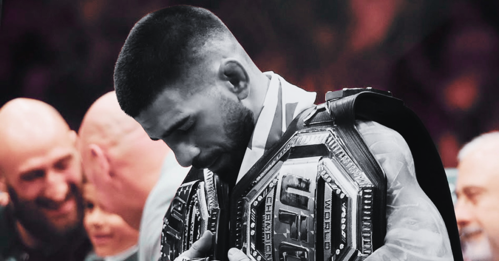 Ilia Topuria, campeón de UFC, sostiene su cinturón mirando hacia abajo con expresión pensativa tras su victoria en MMA.