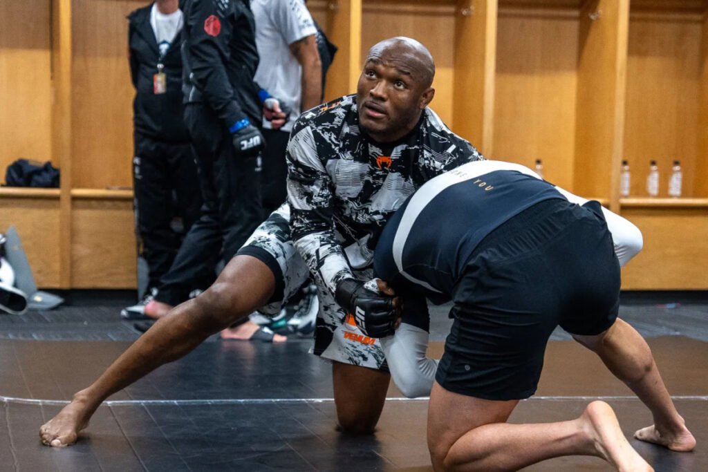 Kamaru Usman, con guantillas UFC, haciendo grappling en un tatami durante su calentamiento.