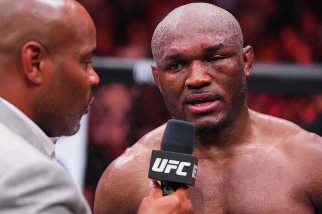 Kamaru Usman, magullado y sudoroso, es entrevistado por Daniel Cormier con micrófono UFC tras su derrota.