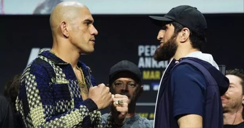 Careo intenso entre dos luchadores de MMA, uno calvo con chaqueta de cuadros, y otro barbudo con gorra negra y puños cerrados.