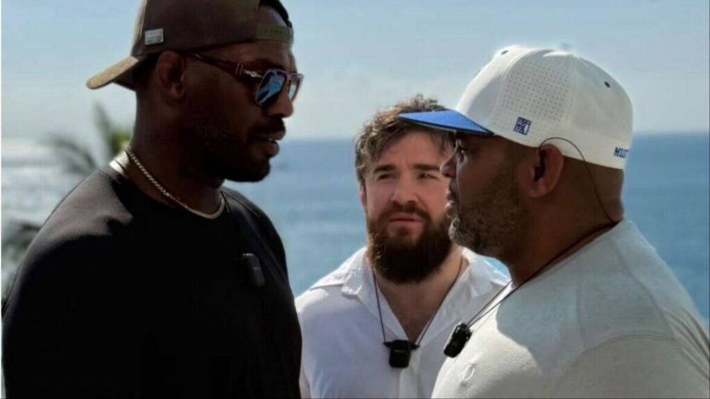 Jon Jones y Daniel Cormier, con un tercer hombre, charlan con micrófonos al aire libre junto al mar.