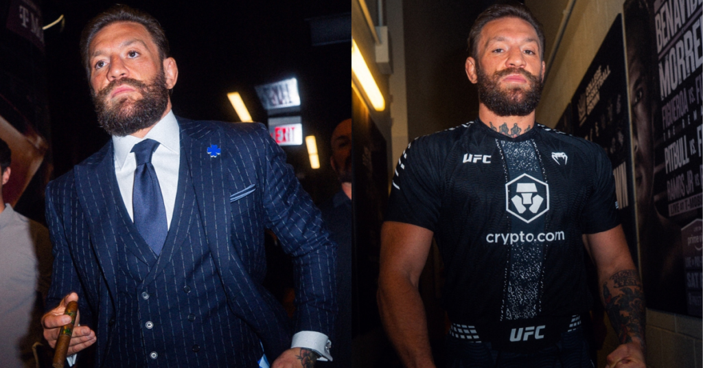 Conor McGregor con traje a rayas azul oscuro y puro, y a su lado con camiseta negra de UFC.