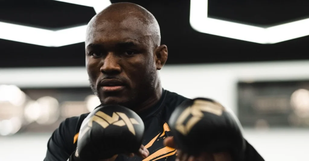 Kamaru Usman, el luchador de MMA, luce sudoroso con guantes negros y dorados, mostrando una mirada concentrada en su entrenamiento.