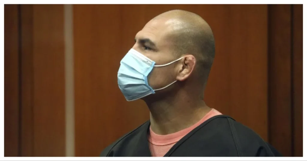 Cain Velasquez, luchador MMA, de perfil con mascarilla azul y oreja de coliflor, en un entorno judicial.