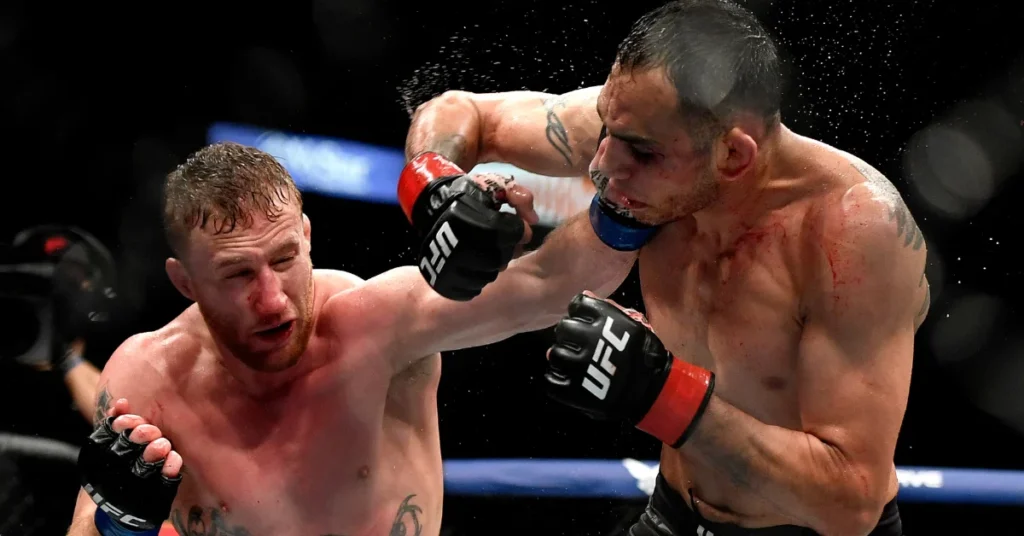Dos luchadores de UFC en plena acción: uno golpea el rostro del otro, salpicando sangre y sudor en el intenso combate MMA.