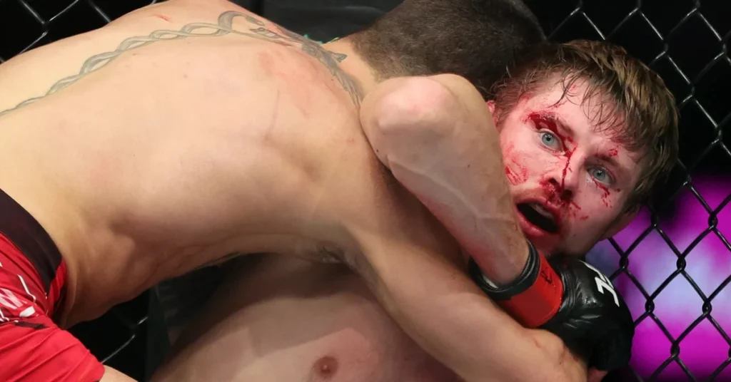 Combate de MMA: luchador ensangrentado con expresión de dolor atrapado por su oponente en la jaula.