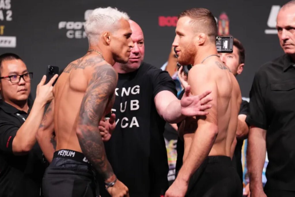 Careo intenso de UFC: Charles Oliveira (pelo platino, tatuajes) y Justin Gaethje se miran fijamente, con Dana White entre ellos.
