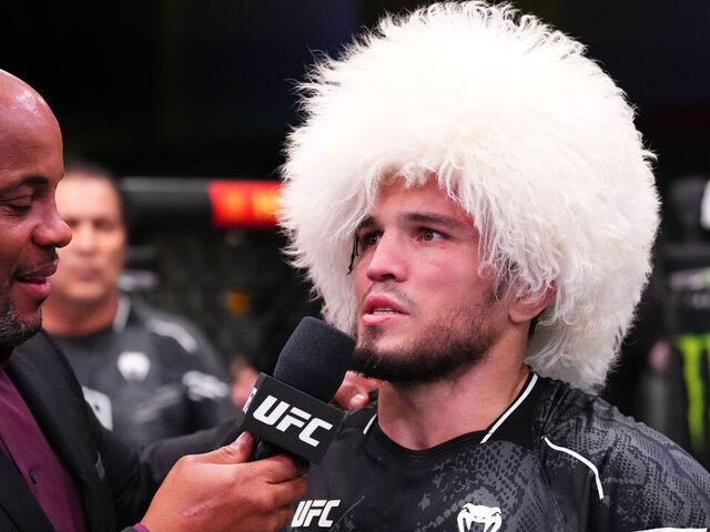 Islam Makhachev con papakha blanca y camiseta de combate, herido, entrevistado por Daniel Cormier de UFC.