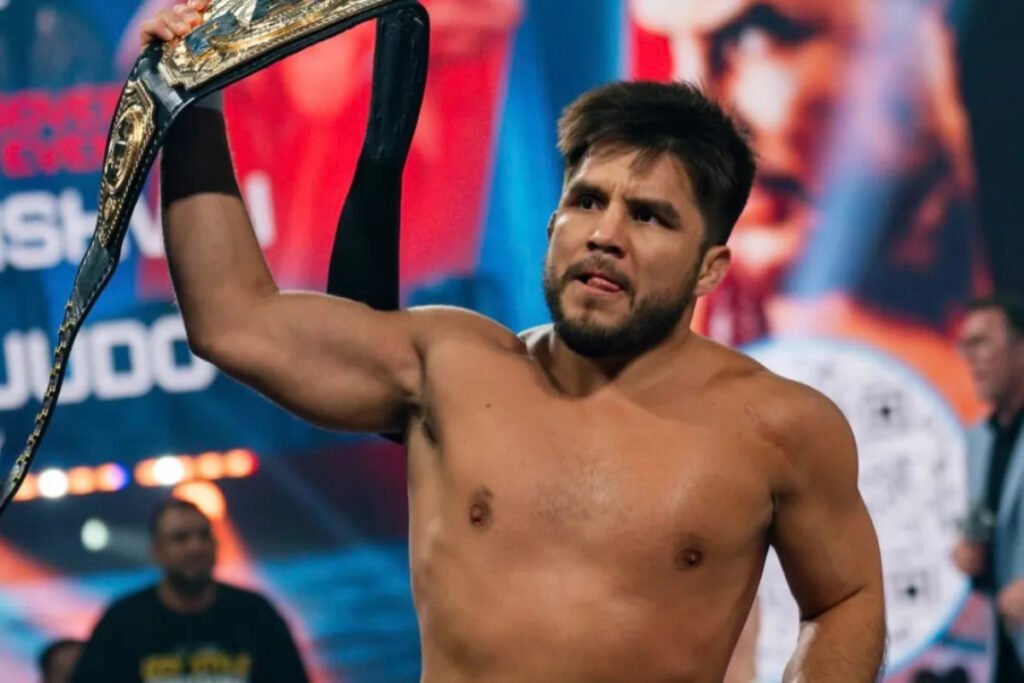 Henry Cejudo, peleador de MMA sin camiseta, celebra su victoria levantando el cinturón de campeón con gesto confiado.