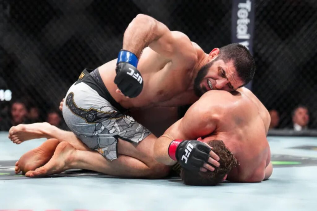 Islam Makhachev domina a Jack Della Maddalena en el suelo del octágono UFC. El luchador barbudo está en posición de golpeo.