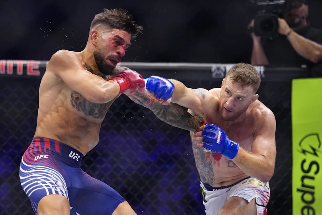 Justin Gaethje (guantes azules) asesta un derechazo a Ilia Topuria (guantes rojos) en un combate de MMA; Topuria sangra. UFC.