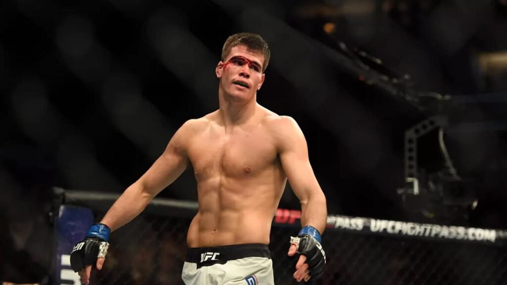 Luchador MMA del UFC con corte sangriento sobre el ojo izquierdo y protector bucal, de pie en el octágono tras un combate.