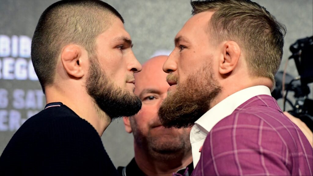 Khabib Nurmagomedov y Conor McGregor en un intenso careo UFC. Luchadores con barbas, orejas de coliflor; Dana White de fondo.