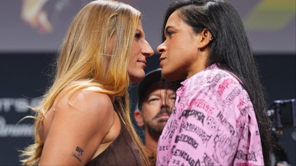Dos luchadoras de UFC, una rubia y otra morena, se enfrentan cara a cara en un tenso careo.