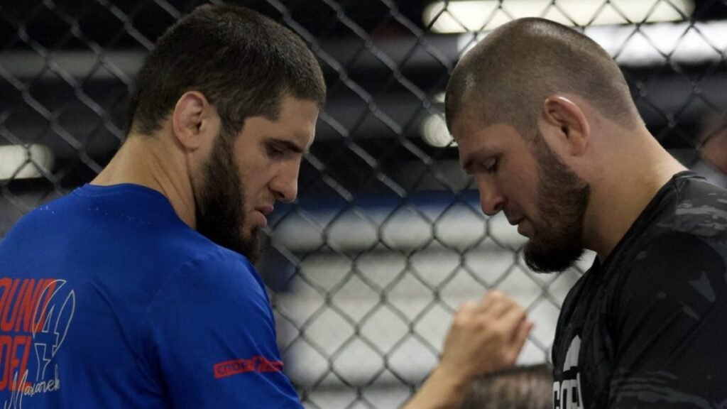Islam Makhachev y Khabib Nurmagomedov cara a cara en jaula de MMA, cabizbajos, durante entrenamiento.