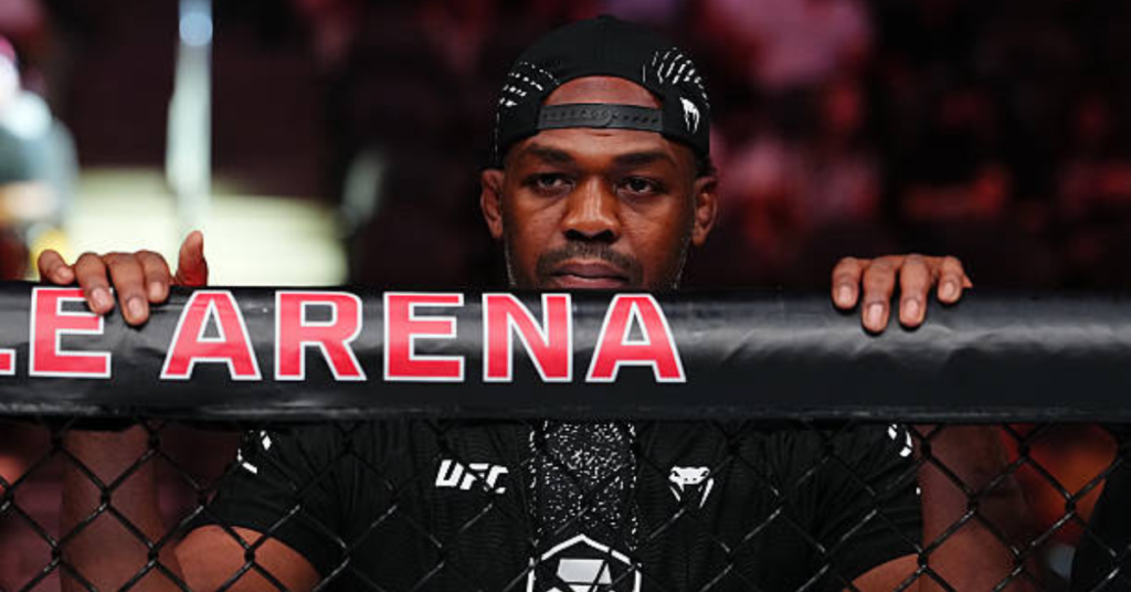 Jon Jones, estrella de la UFC, asoma la cabeza por encima de la jaula del octágono con mirada concentrada, vistiendo de negro.