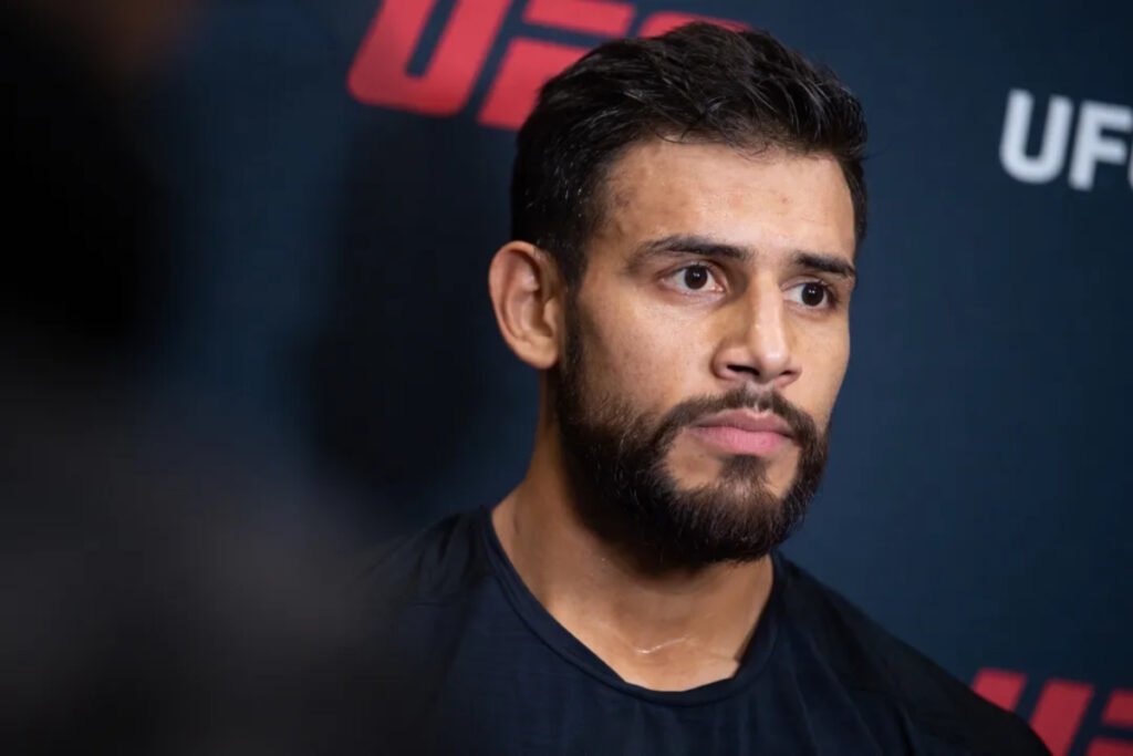 Yair Rodríguez, luchador de UFC, con barba y expresión reflexiva. Primer plano durante una conferencia de prensa con el logo de UFC.