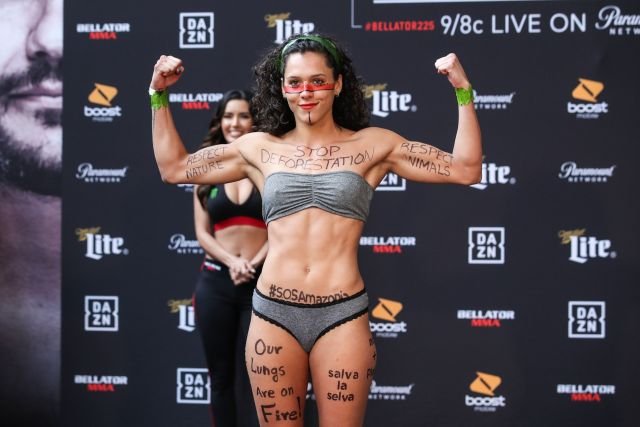 Atleta flexiona en pesaje Bellator, con cuerpo pintado: "STOP DEFORESTATION", "#SOSAmazonia". Protesta ecológica por la Amazonia.