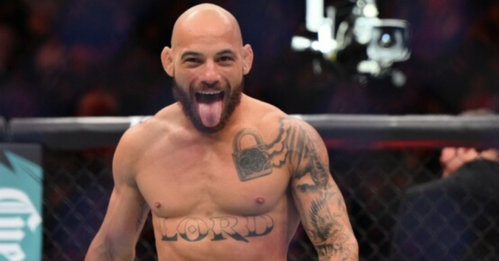 Luchador de MMA calvo y barbudo, tatuado con candado, saca la lengua y celebra eufórico en el octágono.