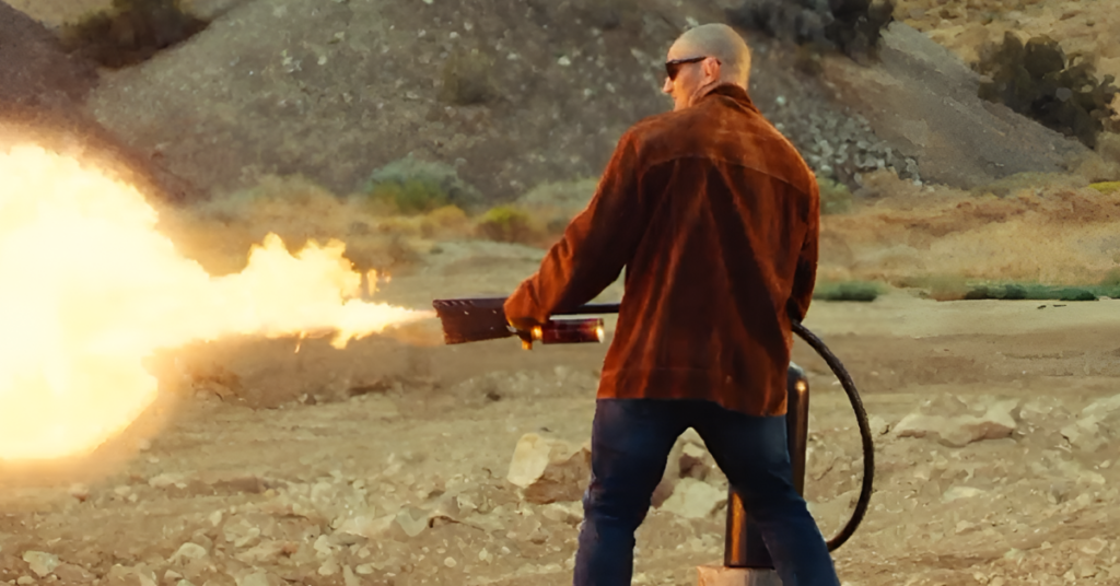 Sean Strickland con lanzallamas despidiendo fuego intenso en paisaje árido y rocoso.