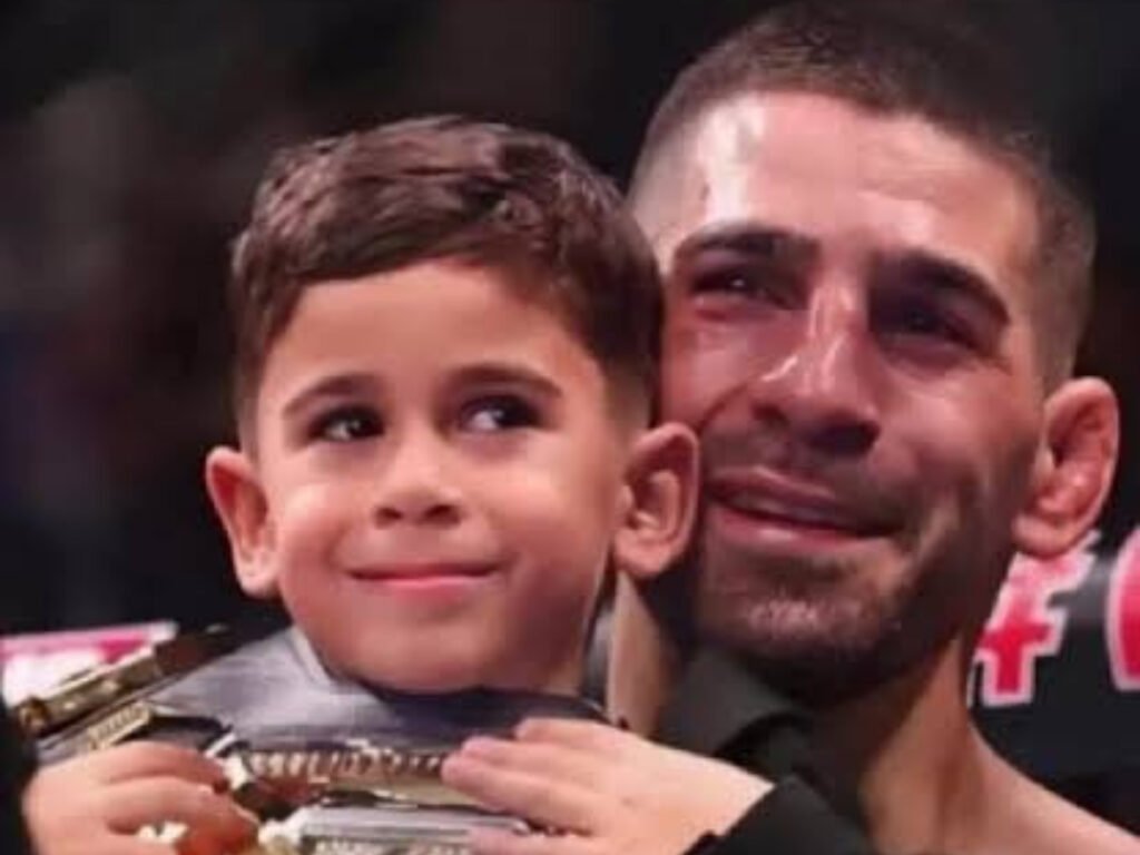 Ilia Topuria, emocionado y con lágrimas, abraza a su hijo sonriente que sostiene un cinturón de campeón de la UFC.